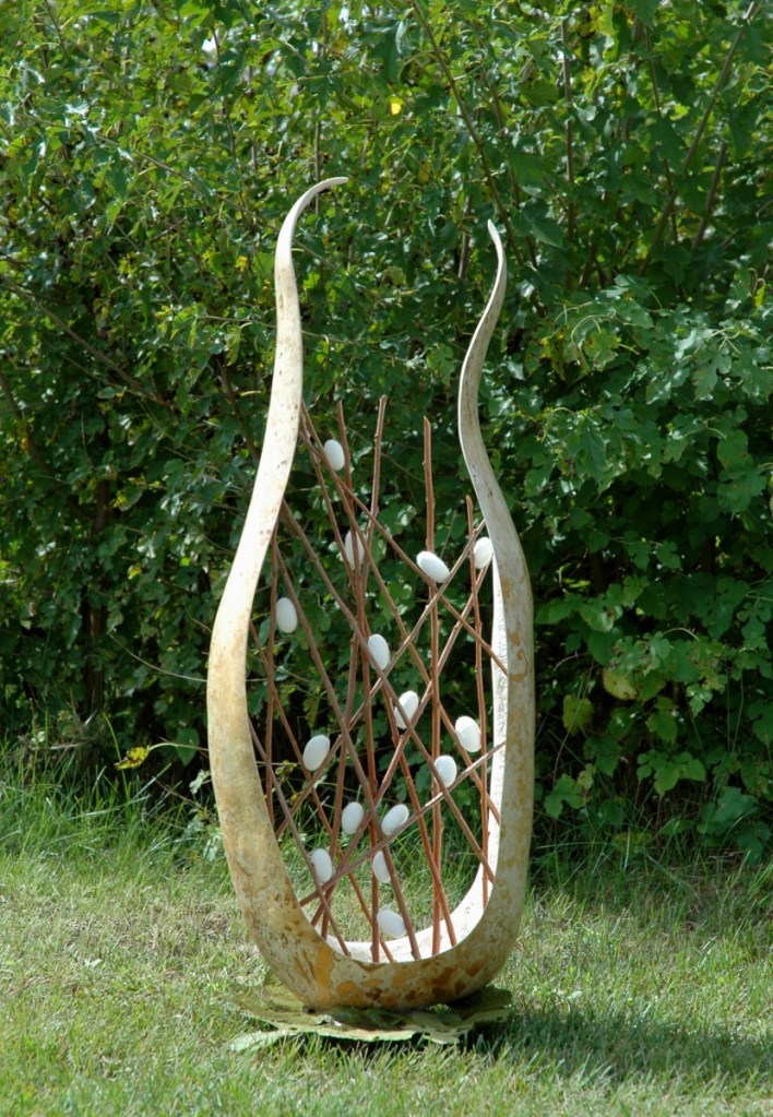 Sculptural artwork with silk cocoons and branches inside a carved gourd.